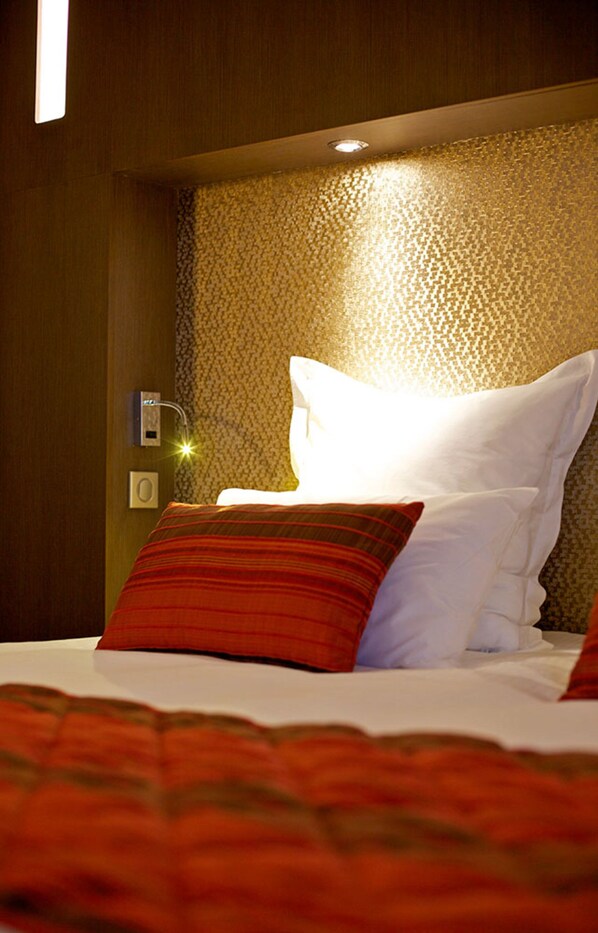 A hotel room with a bed, a nightstand, and a wall-mounted light fixture.