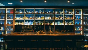A bar area with multiple shelves of liquor bottles, a bar counter, and several chairs.