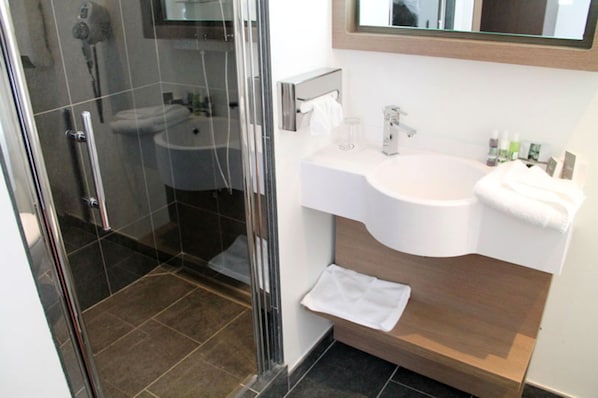 A modern bathroom with a glass shower enclosure, a white sink, and a wooden vanity.