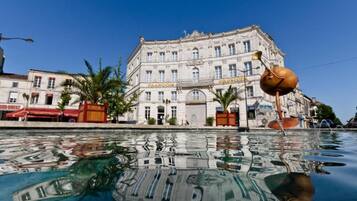Stunning historic building with a classical facade, situated beside a serene body of water, featuring a unique sculpture in the foreground.