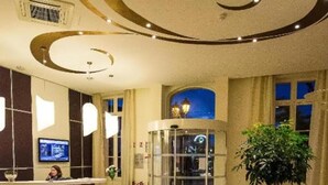 A hotel lobby with a reception desk, a glass elevator, a large potted plant, and a circular seating area.