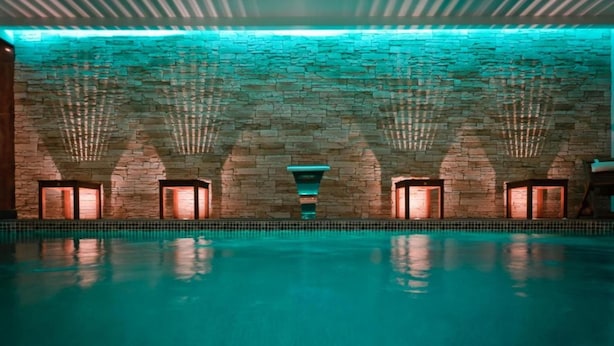 A swimming pool with stone walls and multiple archways, illuminated by warm lighting.