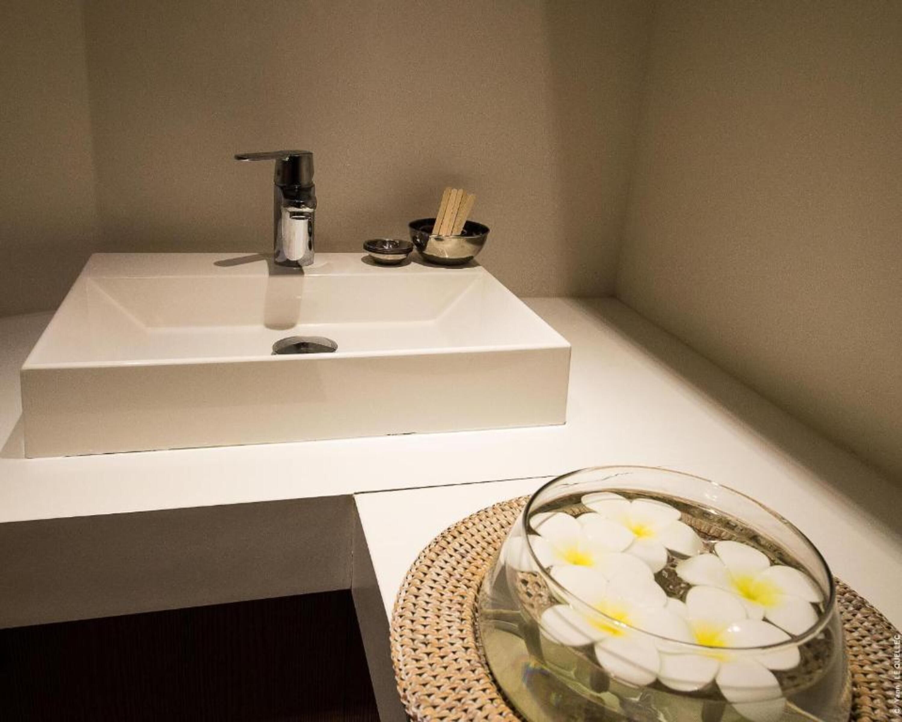 A bathroom with a white sink, a glass bowl with white flowers, and a small container with chopsticks.