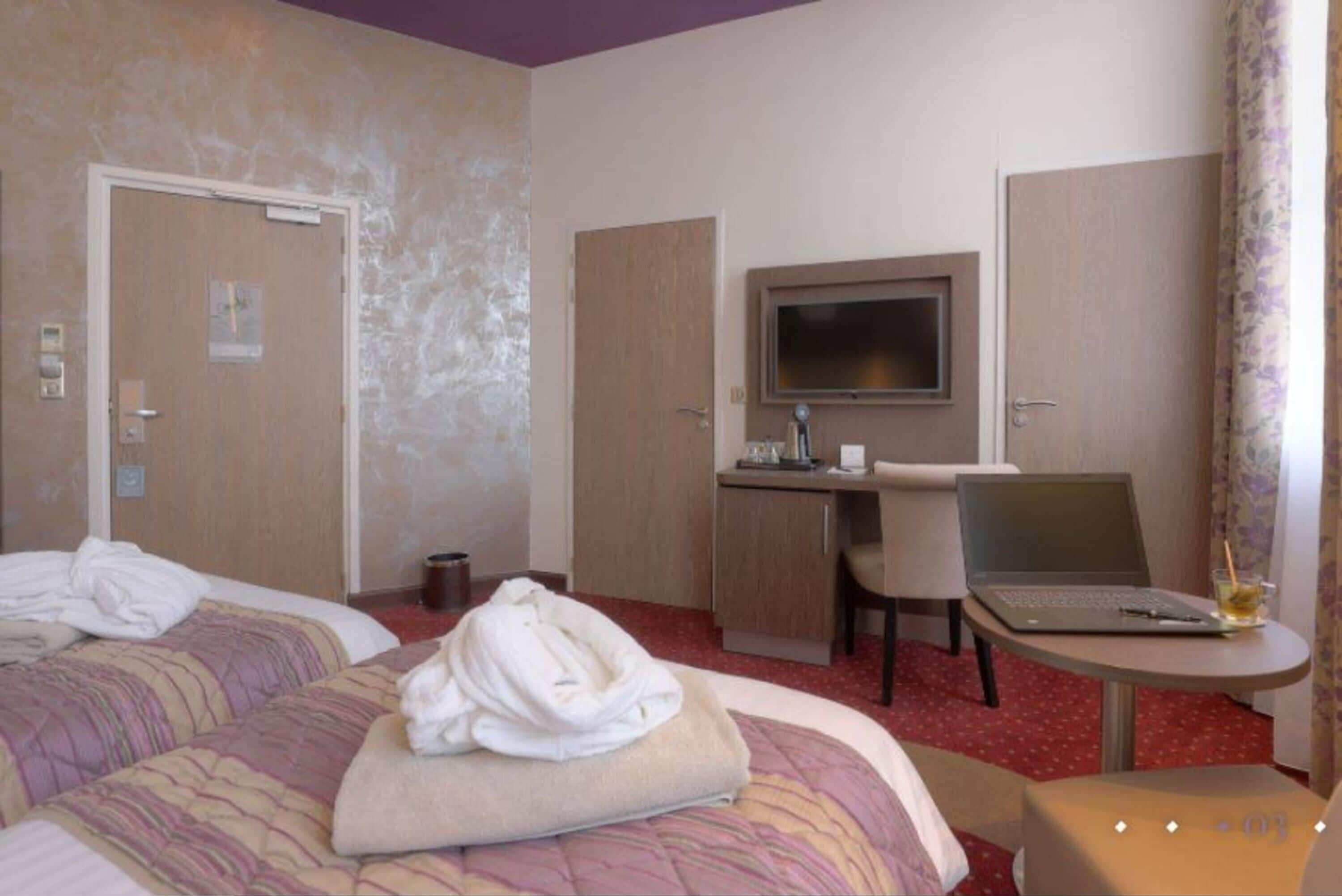 Une chambre d’hôtel avec deux lits, un bureau avec un ordinateur portable, une télévision et une petite table avec une boisson.