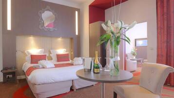 Habitación de hotel con cama, mesitas de noche, una mesa redonda con una silla y un florero con flores.