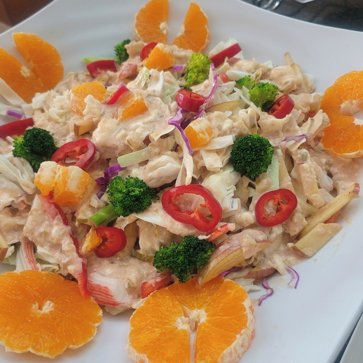 Une assiette de salade de poulet, accompagnée de brocolis et de tranches d'orange.