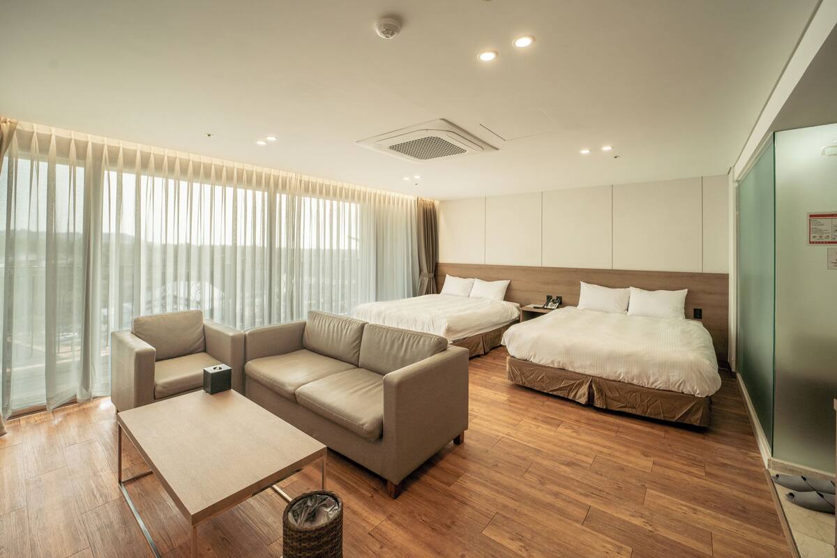 A hotel room with a sofa, a bed, a small table, and a view of the outdoors.