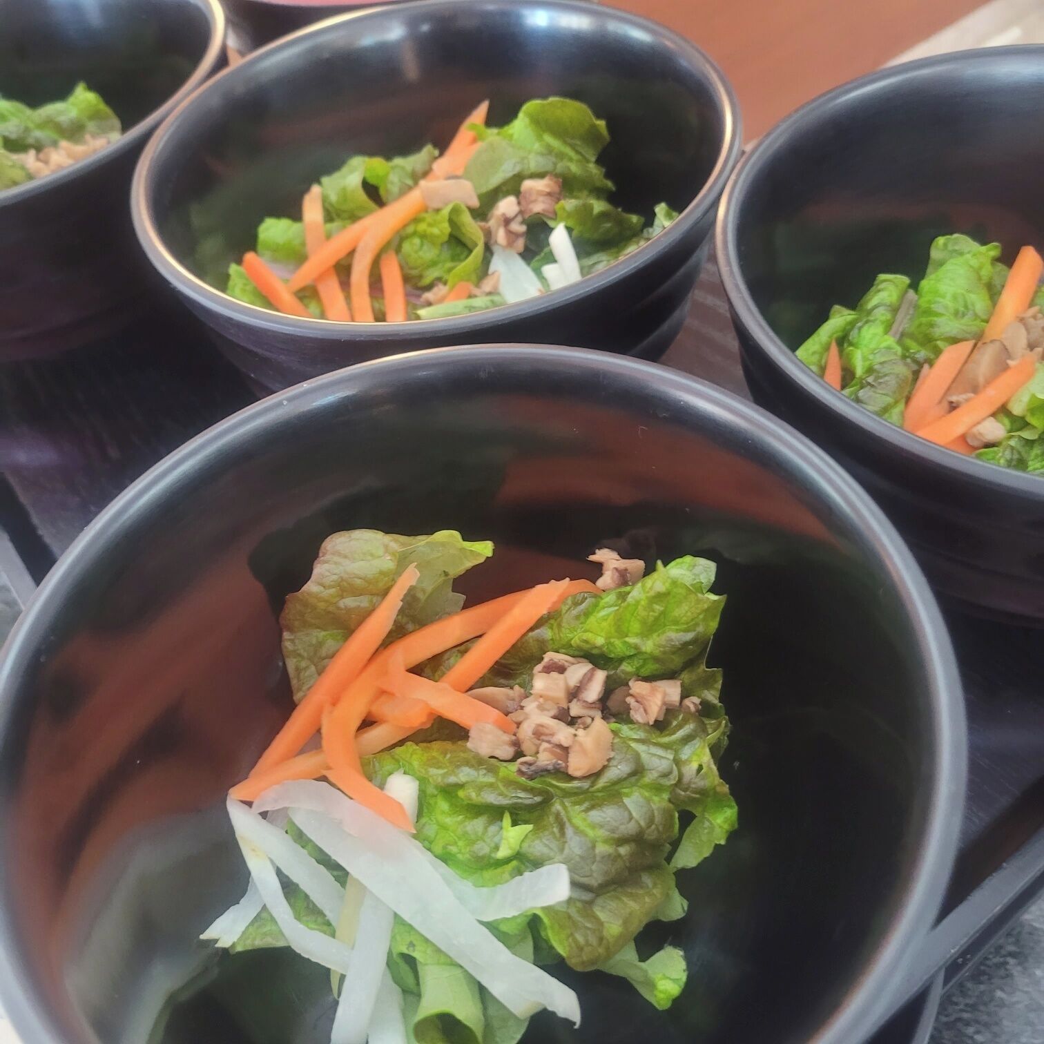 A series of black bowls containing a salad with lettuce, shredded carrots, and a protein.