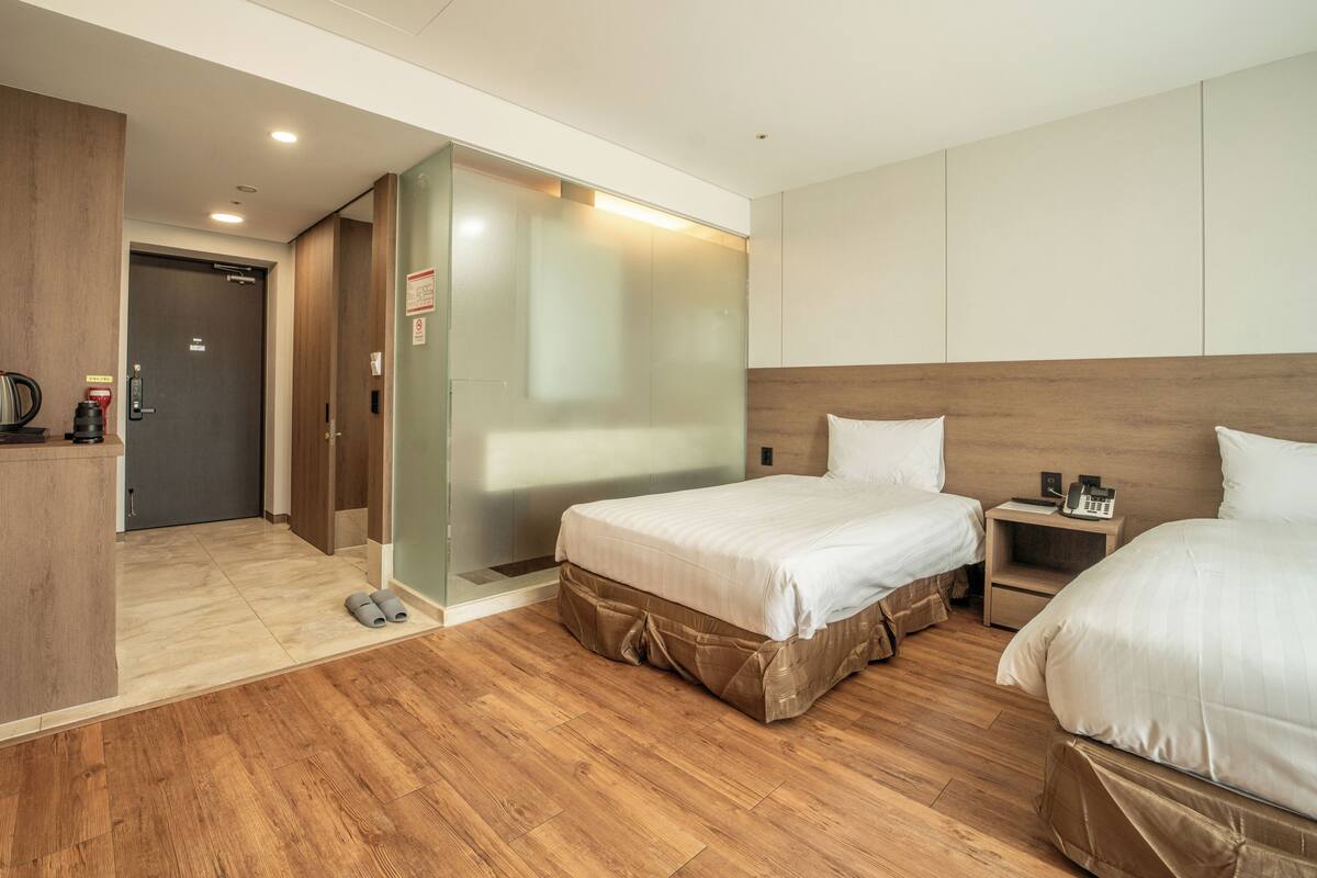 A hotel room with two beds, a wooden floor, a minibar, and a sliding door.