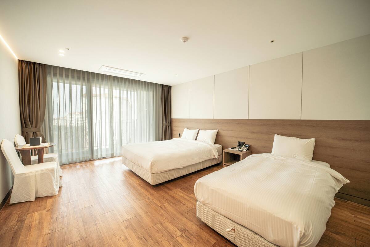 A hotel room with two beds, a desk, a chair, and a large window with curtains.
