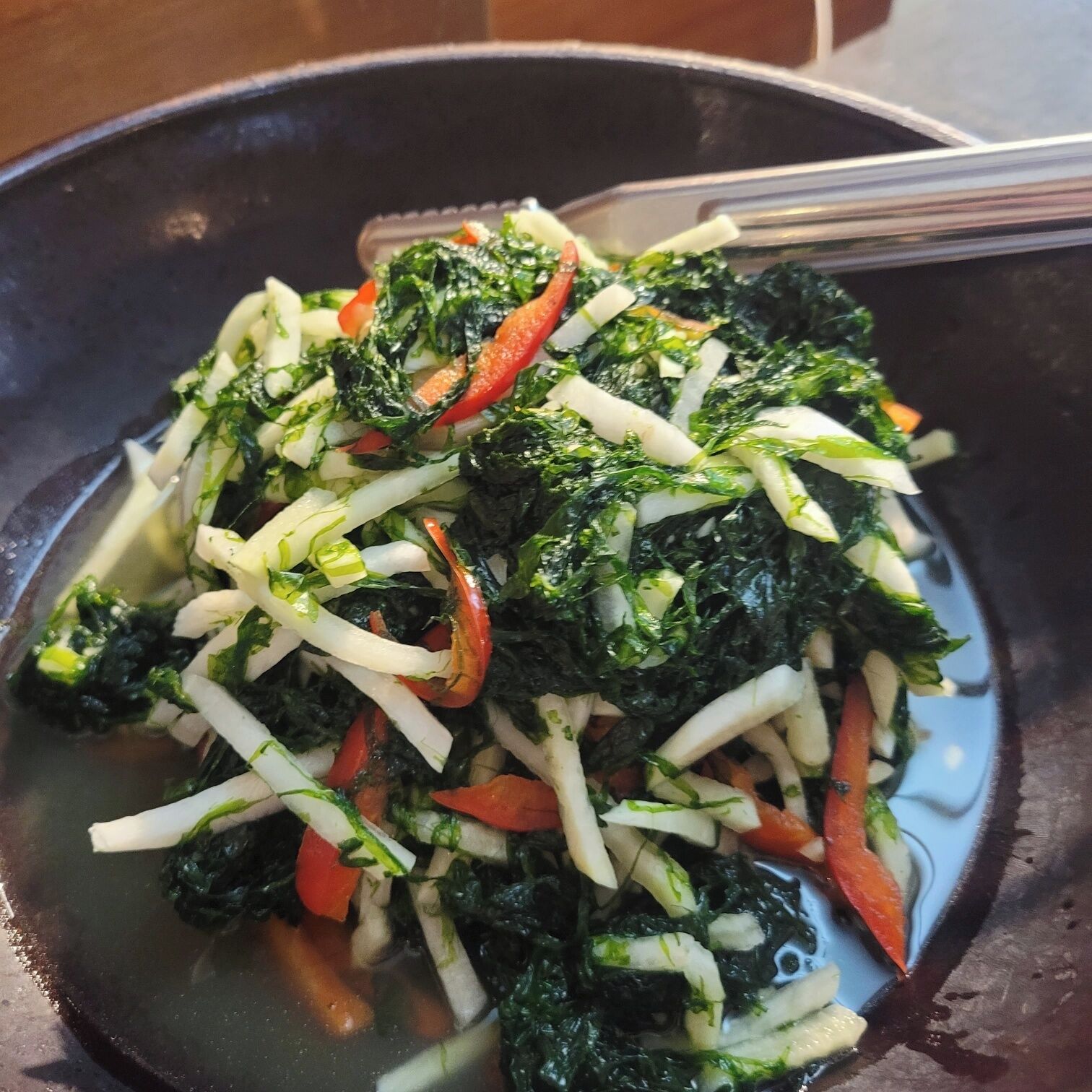 Una wok con un salteado que contiene verduras de hoja, zanahorias y quizás otros vegetales.