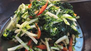 Una wok con un salteado que contiene verduras de hoja, zanahorias y quizás otros vegetales.