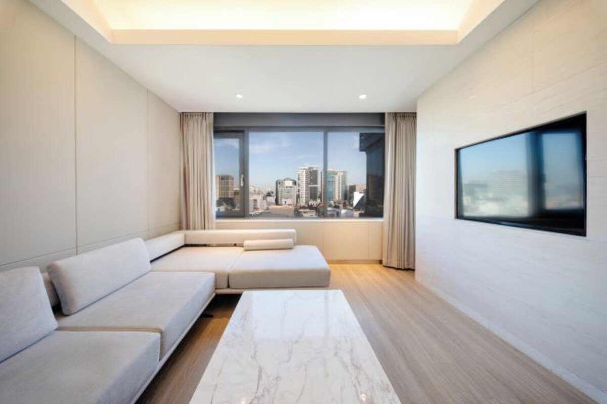 A modern living room with a city view, a large window, and a flat-screen TV mounted on the wall.