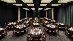 Un amplio salón de banquetes con mesas redondas dispuestas para cenar, con una lámpara de araña en el centro y vistas del horizonte de la ciudad.