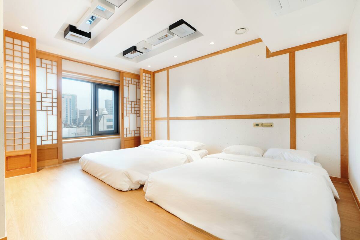 Una habitación de hotel con dos camas, un ventanal grande y un panel de madera tradicional.