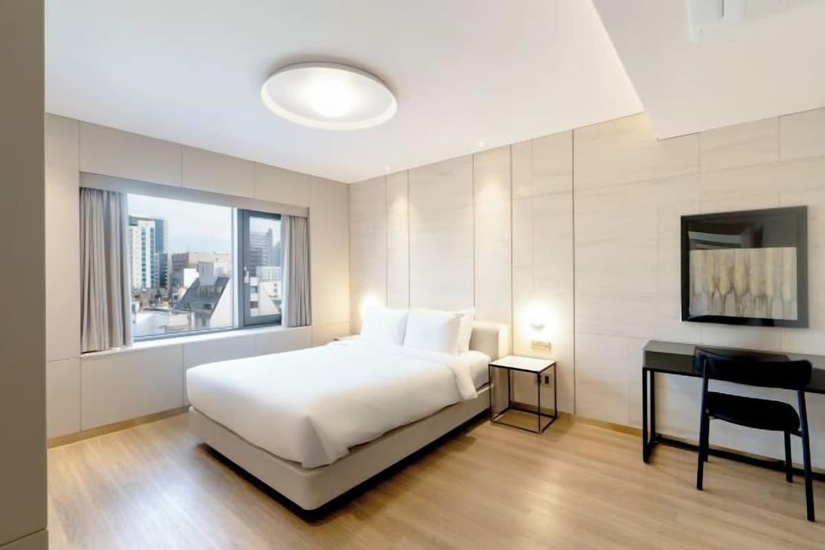 A modern hotel room with a large bed, a desk, and a chair.