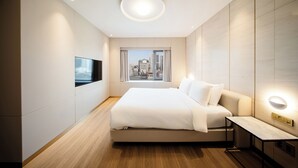 Un dormitorio de hotel moderno con una cama grande, un televisor montado en la pared y vistas a la ciudad a través de la ventana.