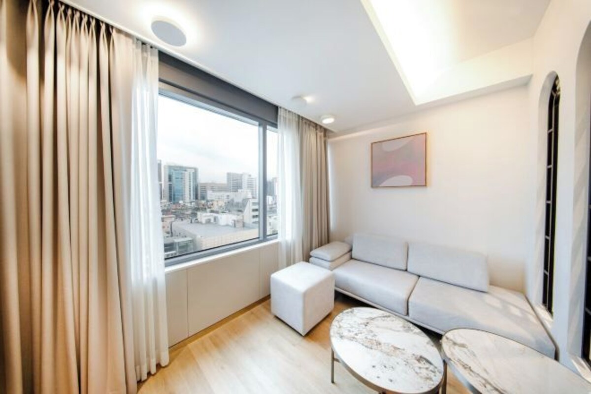 A modern living room with a large window, a sofa, and two marble coffee tables.