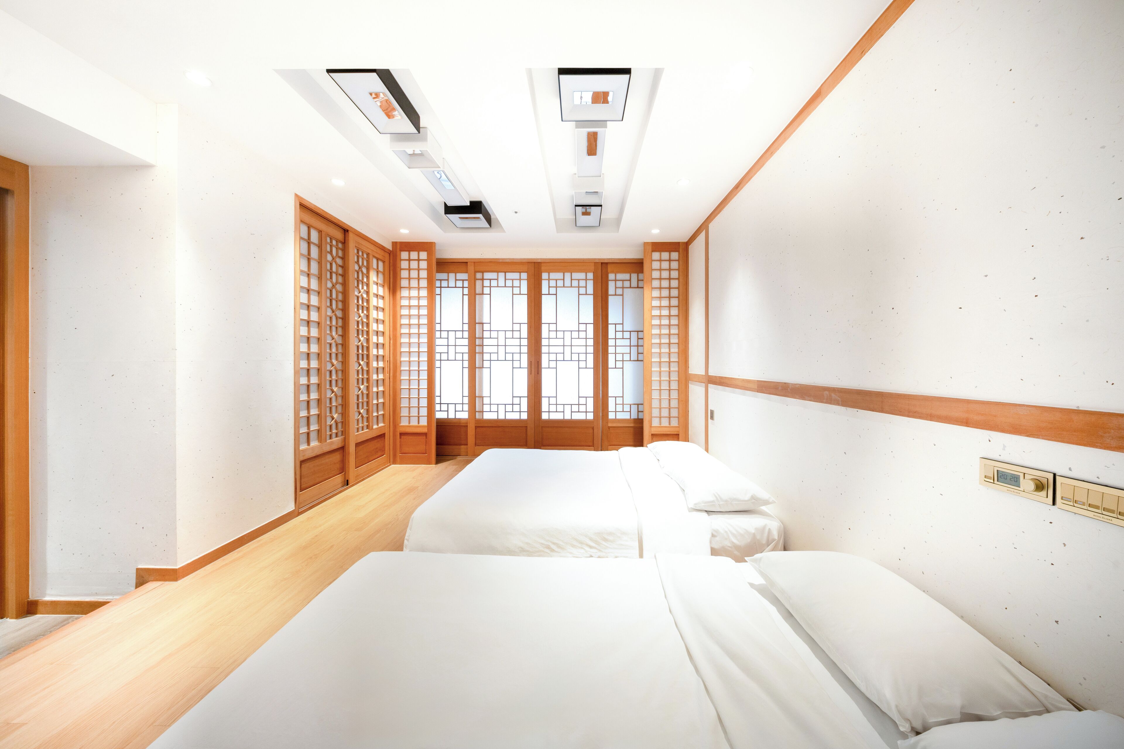 Une chambre d’hôtel avec deux lits, un plancher en bois, une porte coulissante traditionnelle et un plafond doté d’un éclairage encastré.