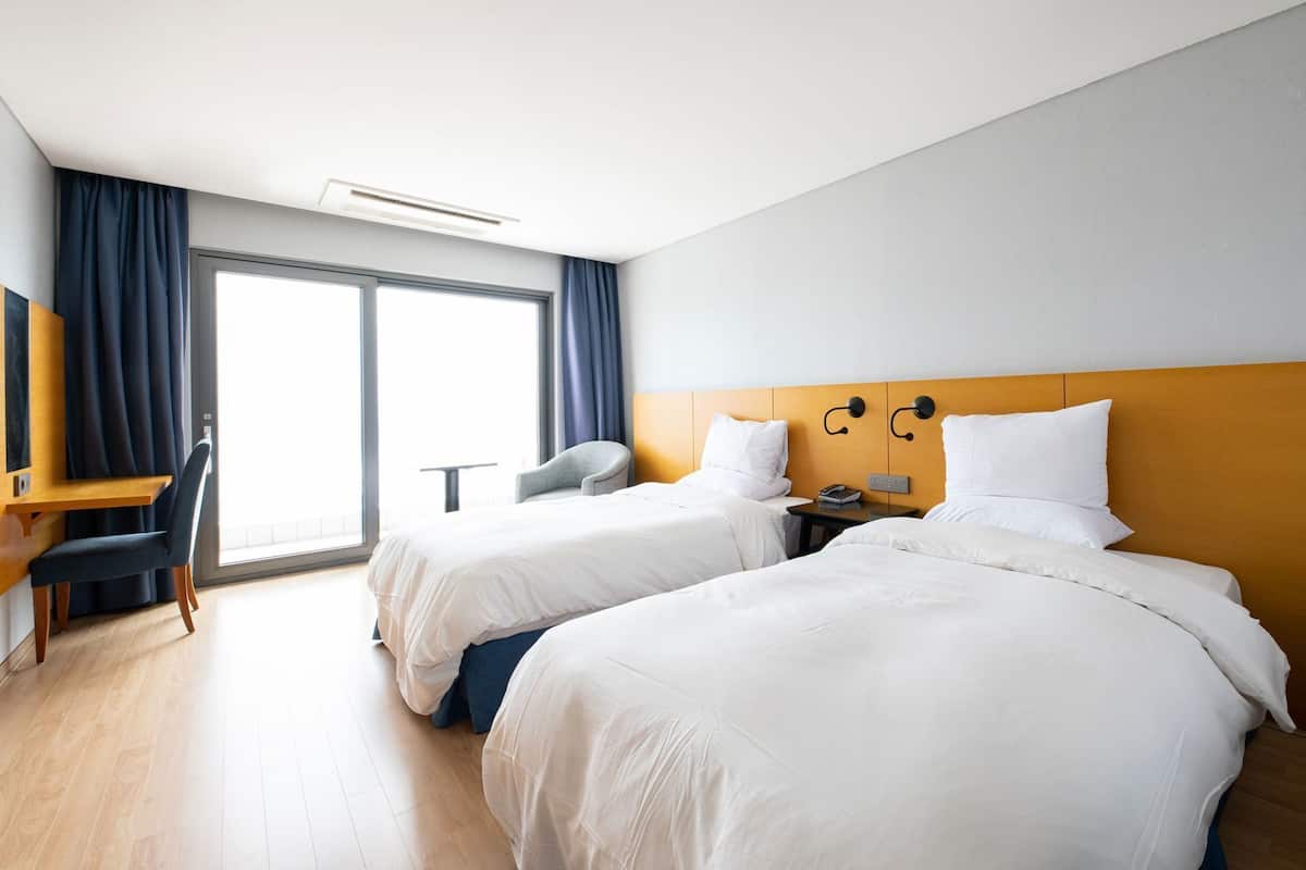 A hotel room with two beds, a desk, a chair, a TV, and a large window.