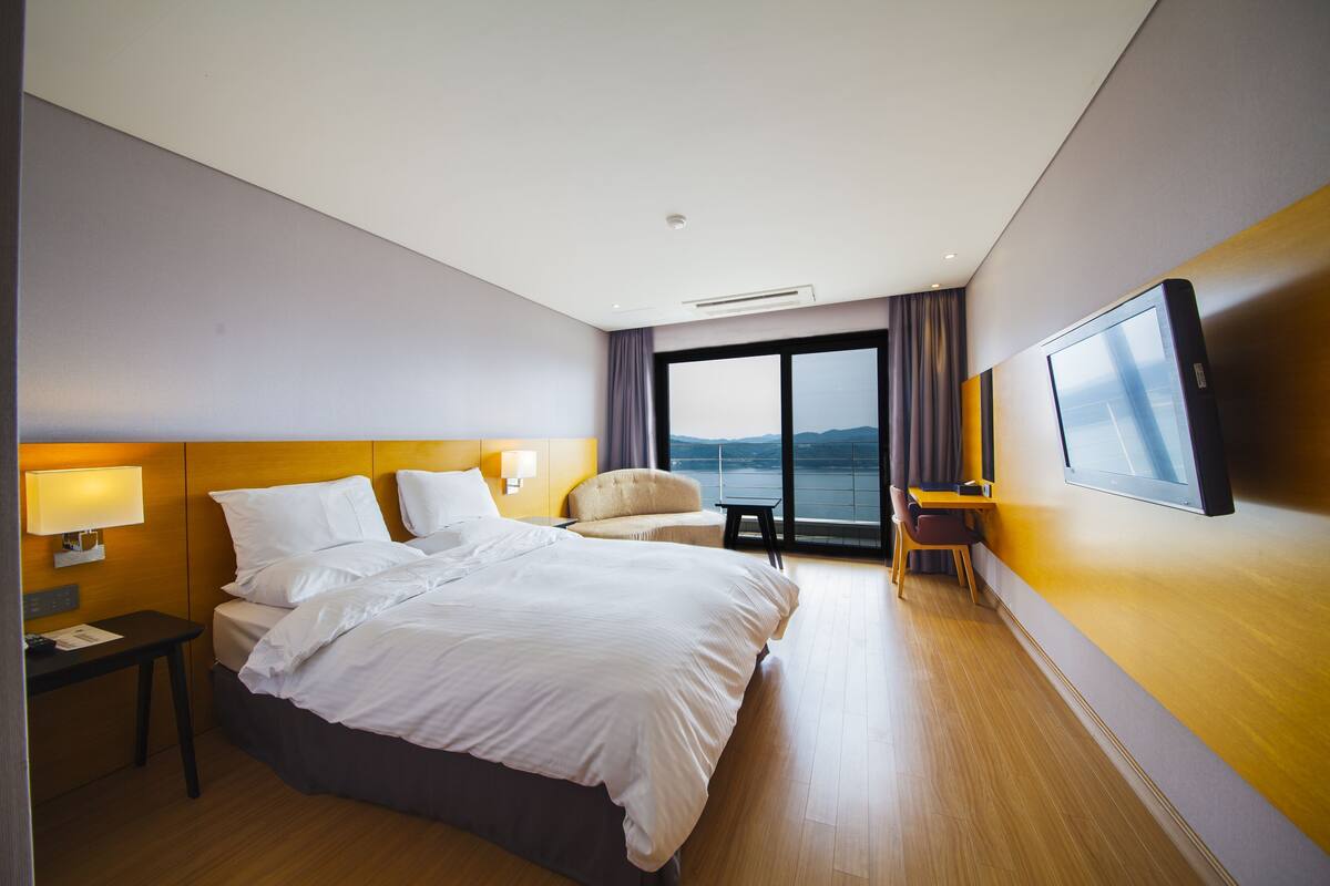 A hotel room with a large bed, a desk, a chair, a TV, and a view of the outdoors.