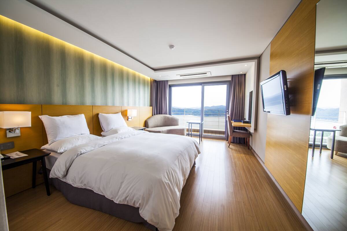 A modern hotel room with a large bed, a desk, a chair, and a TV.