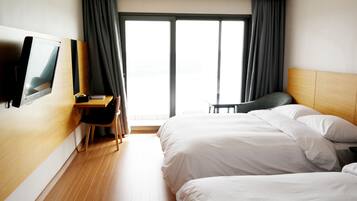 Une chambre d’hôtel avec deux lits, un bureau, une chaise, une télévision et une grande fenêtre avec des rideaux.