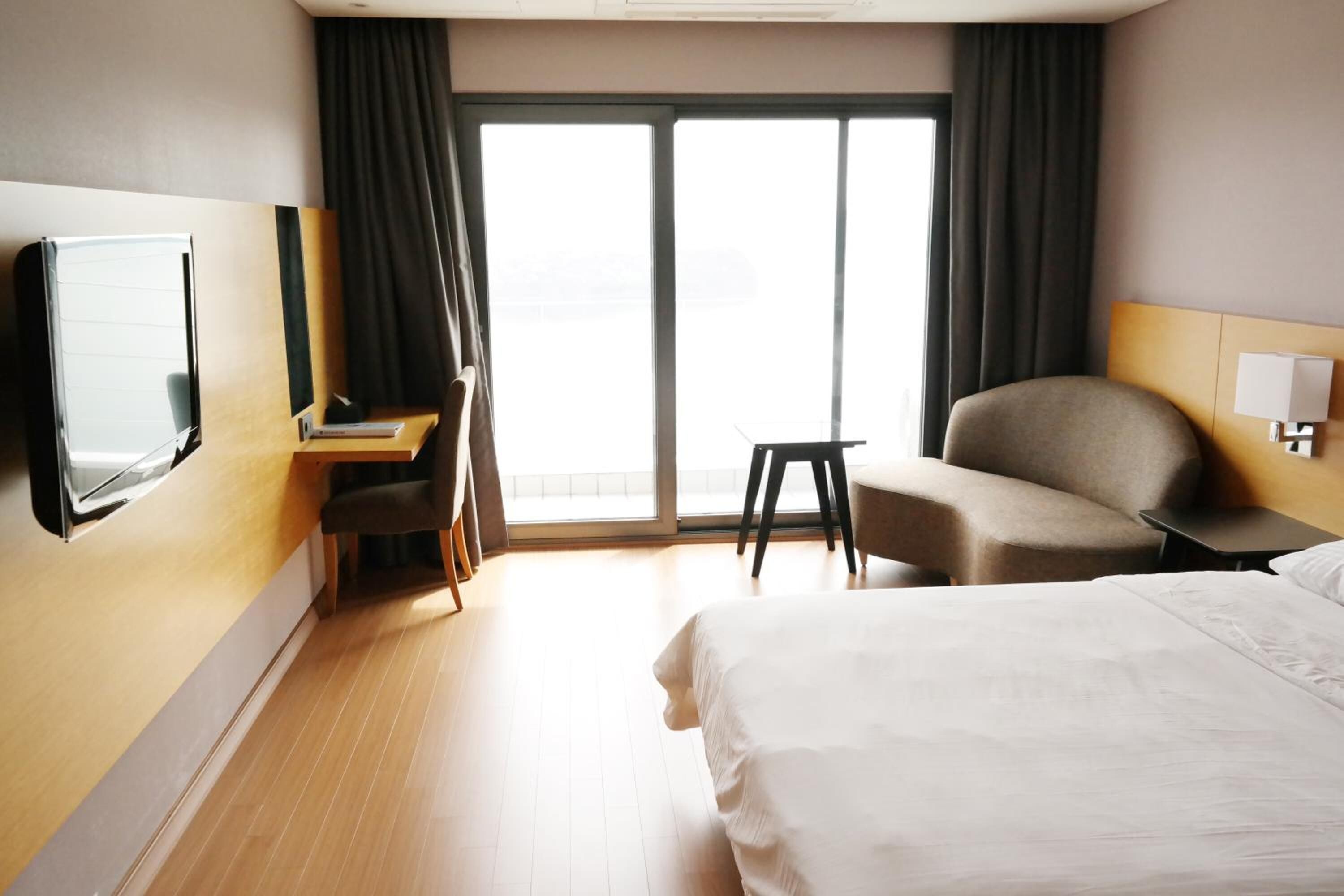 Habitación de hotel con cama, escritorio, silla, televisión y un ventanal grande.