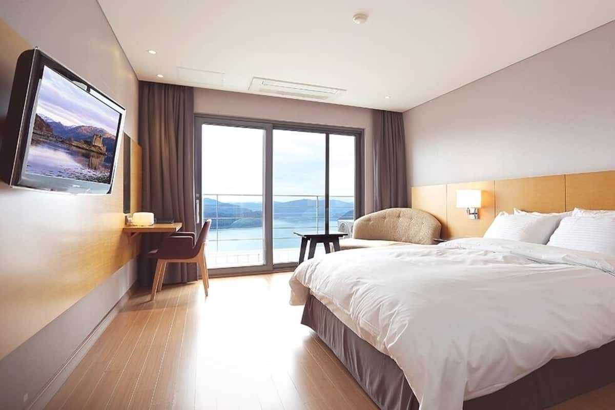 A hotel room with a large bed, a desk, a chair, a TV mounted on the wall, and a view of the outdoors.