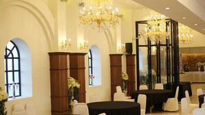 A banquet hall with round tables, white chairs, and chandeliers.