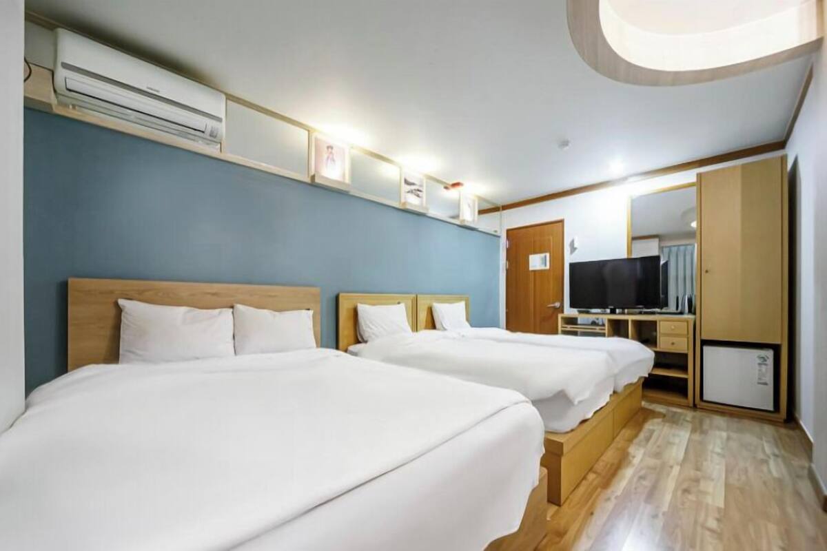 A hotel room with two beds, a TV, a wardrobe, and an air conditioning unit.