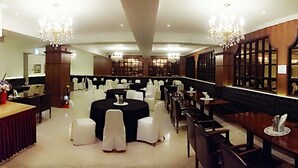 A formal dining area with round tables, white chairs, chandeliers, and wooden paneling.