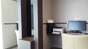 A hotel room with a desk, computer, printer, and a chair.