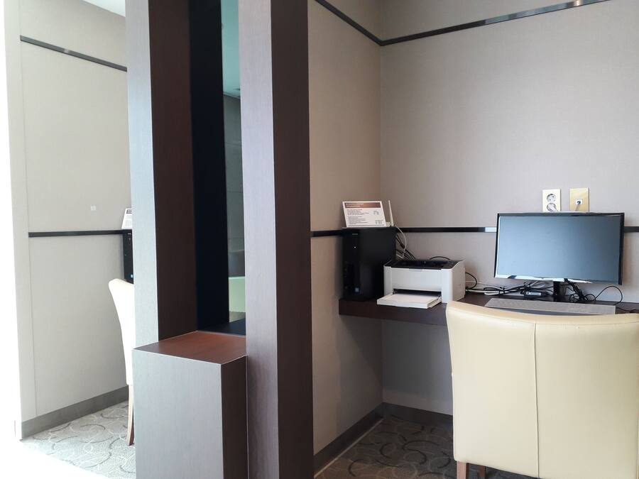 A hotel room with a desk, computer, printer, and a chair.