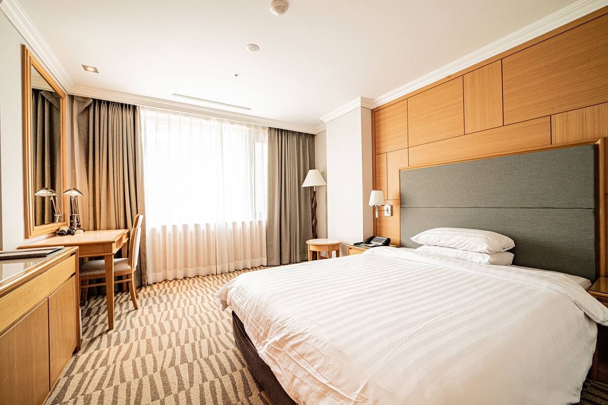 A hotel room with a large bed, a desk with a chair, a small table, and a mirror.