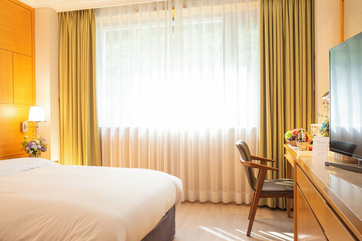 A hotel room with a large bed, a desk with a television, and a window with curtains.