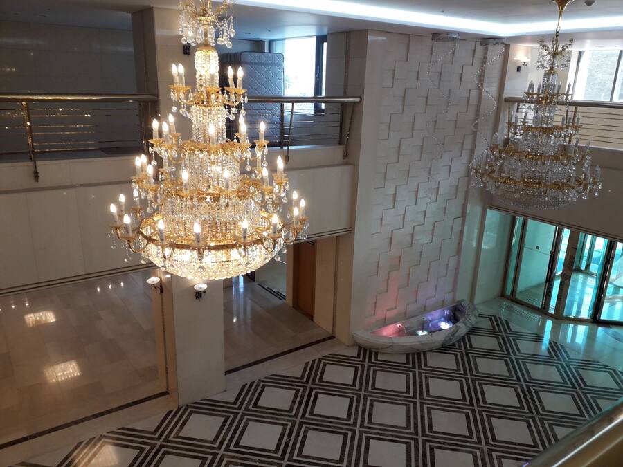 A spacious lobby with a large, ornate chandelier, a patterned floor, and a modern staircase.