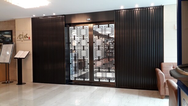 A modern hotel lobby with a reception desk, a menu stand, and a seating area with a massage chair. - Hotel Geumosan (Gumi)