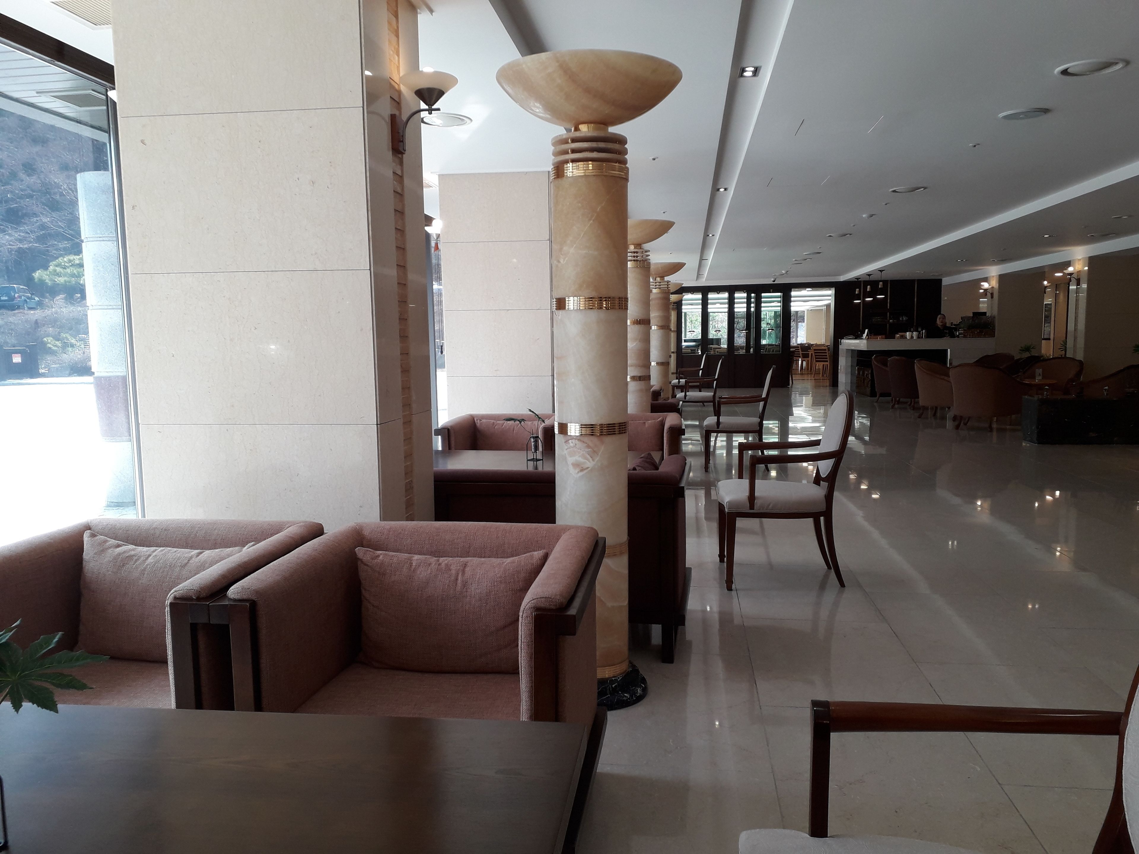 Un hall d’entrée spacieux, doté d’un mobilier moderne, notamment des canapés et des fauteuils, et d’une grande fenêtre offrant une vue sur l’extérieur.