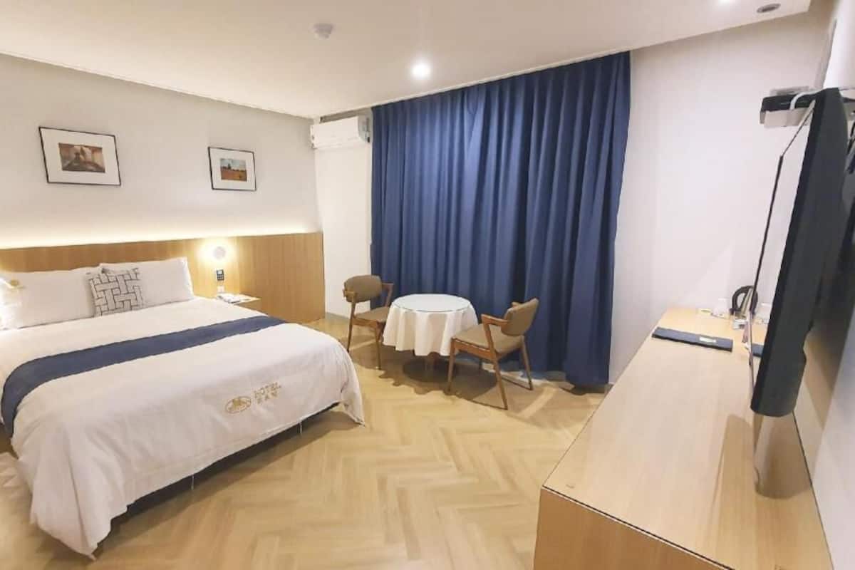 A hotel room with a bed, bedside tables, a desk, chairs, a TV, and curtains.