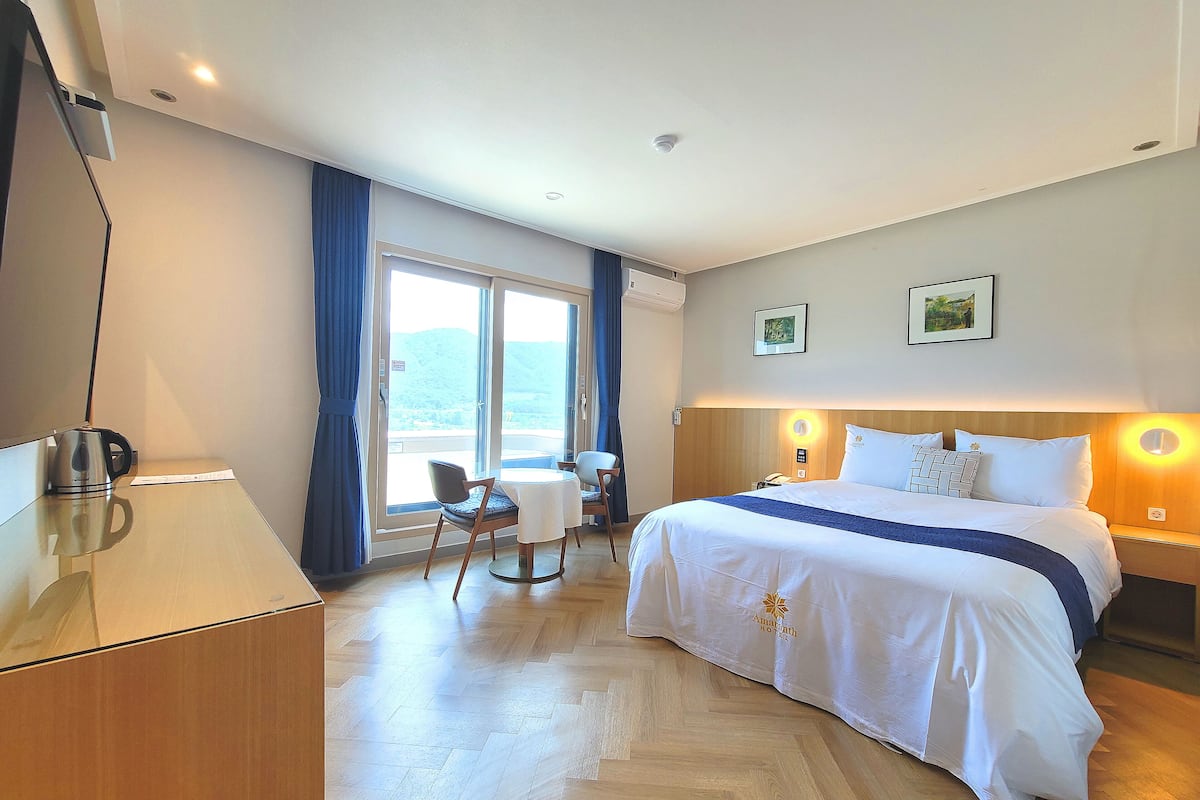 A hotel room with a bed, a desk, a chair, and a view of the outdoors.