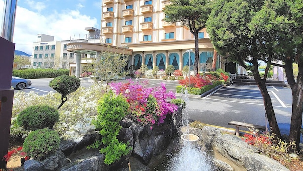 Een hotel met een fontein, weelderige begroeiing en een helderblauwe lucht.