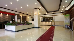 Een hotellobby met een receptiebalie, een rood tapijt en een modern plafondontwerp.