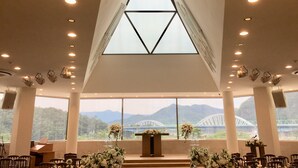Ein Kircheninneres mit hoher Decke, großen Fenstern und Blick auf Berge sowie eine Brücke.