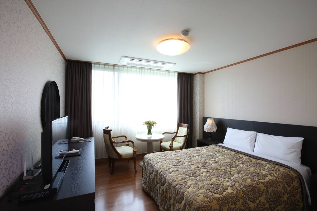 Ein Hotelzimmer mit Bett, Schreibtisch, Stühlen und einem Fenster mit Vorhängen.