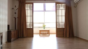 Ein Zimmer mit Holzboden, einem Holztisch mit einer Vase und einem Fenster mit braunen Vorhängen.