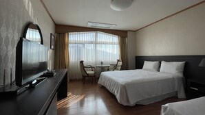 Ein Hotelzimmer mit Bett, Schreibtisch mit Fernseher, Stuhl und Fenster mit Vorhängen.