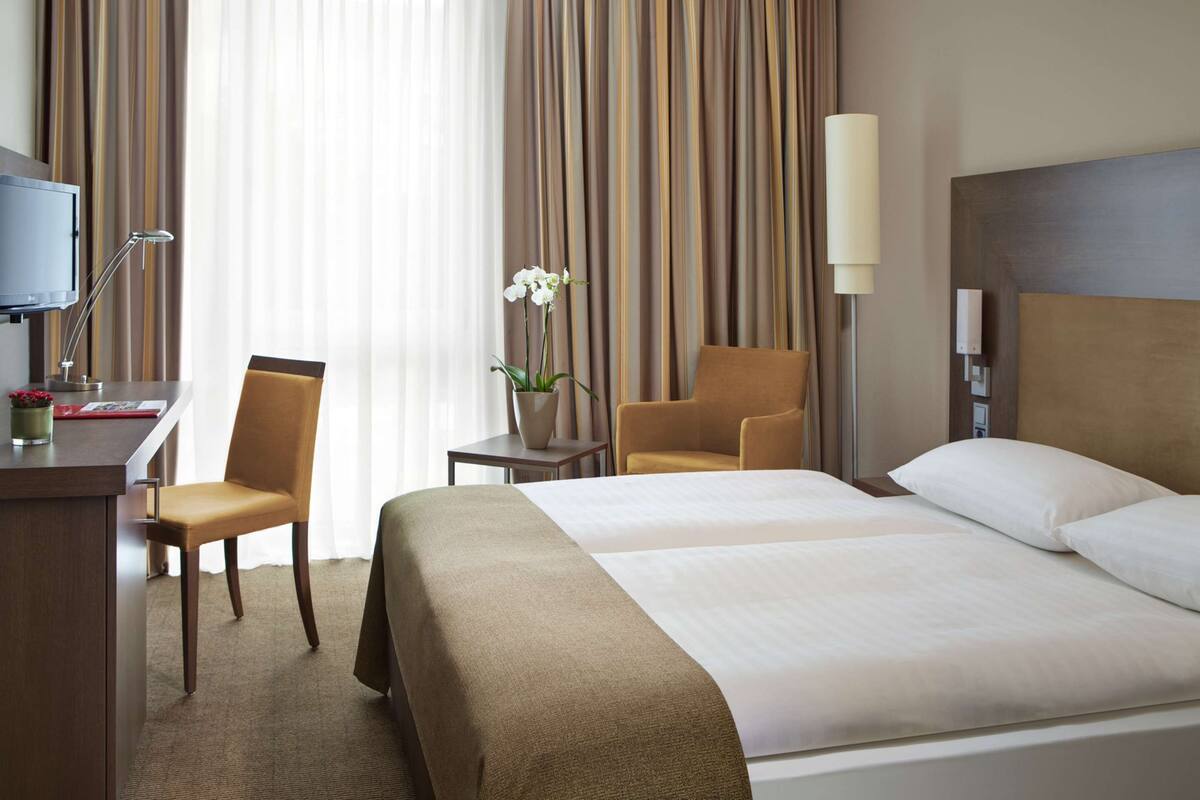 A hotel room with a bed, two chairs, a desk, a TV, and a lamp.