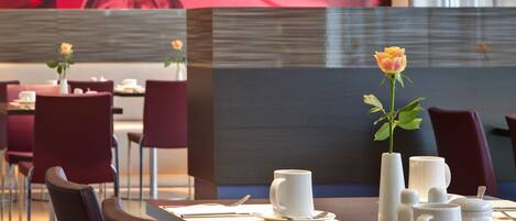 A modern dining area with red floral wall art, a vase with a single yellow rose, and a table set with white teacups and saucers.