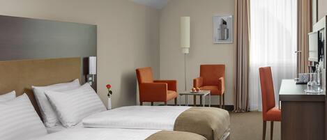 Quarto de hotel com duas camas, uma escrivaninha, uma cadeira e uma televisão.